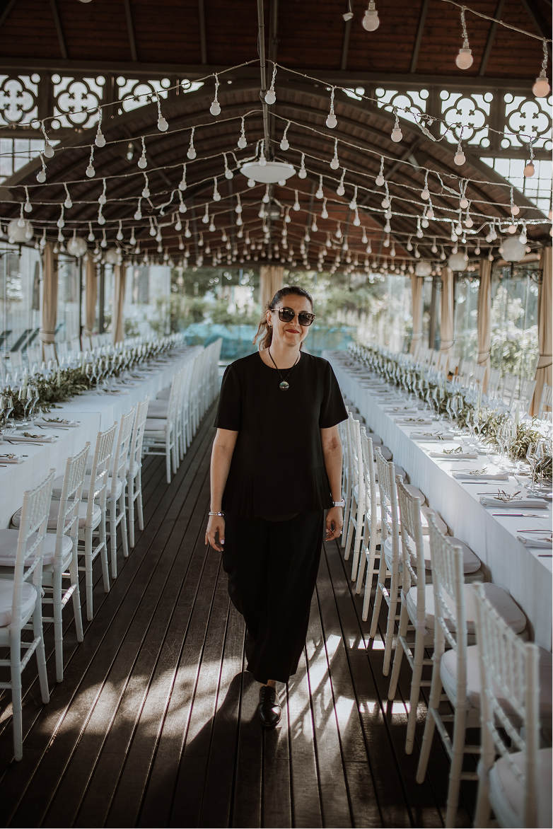Barbara walking between long tables set for a wedding reception under string lights