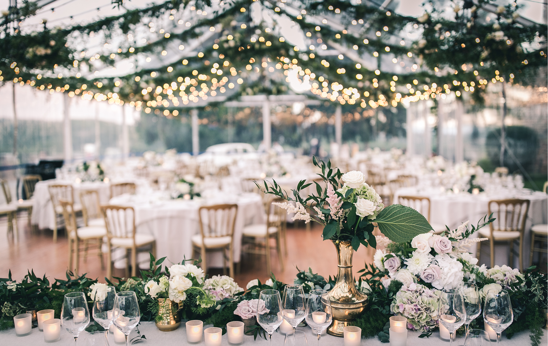 Wedding reception tables under a canopy of string lights and greenery