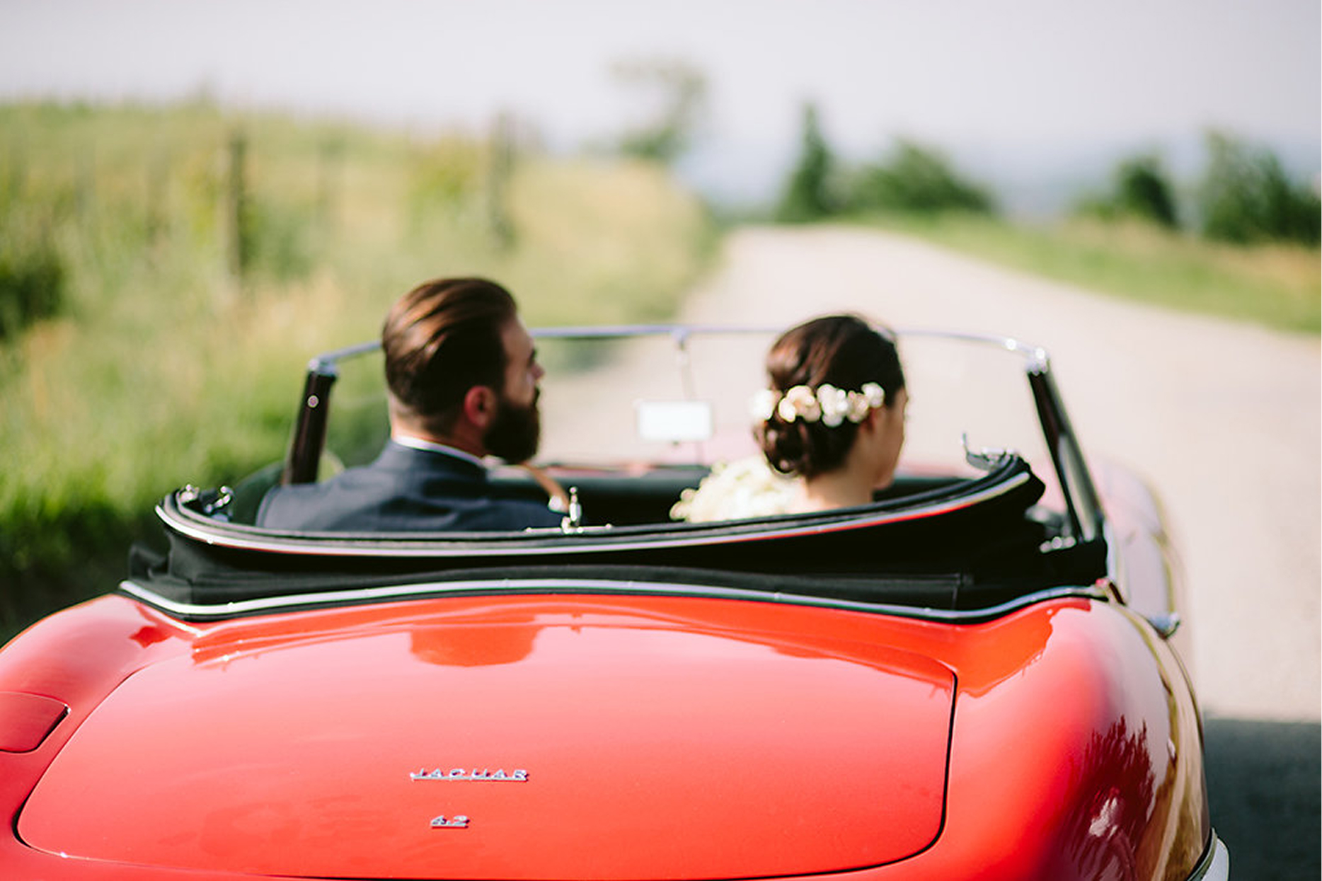 Newlyweds driving away in a red vintage convertible along a country road